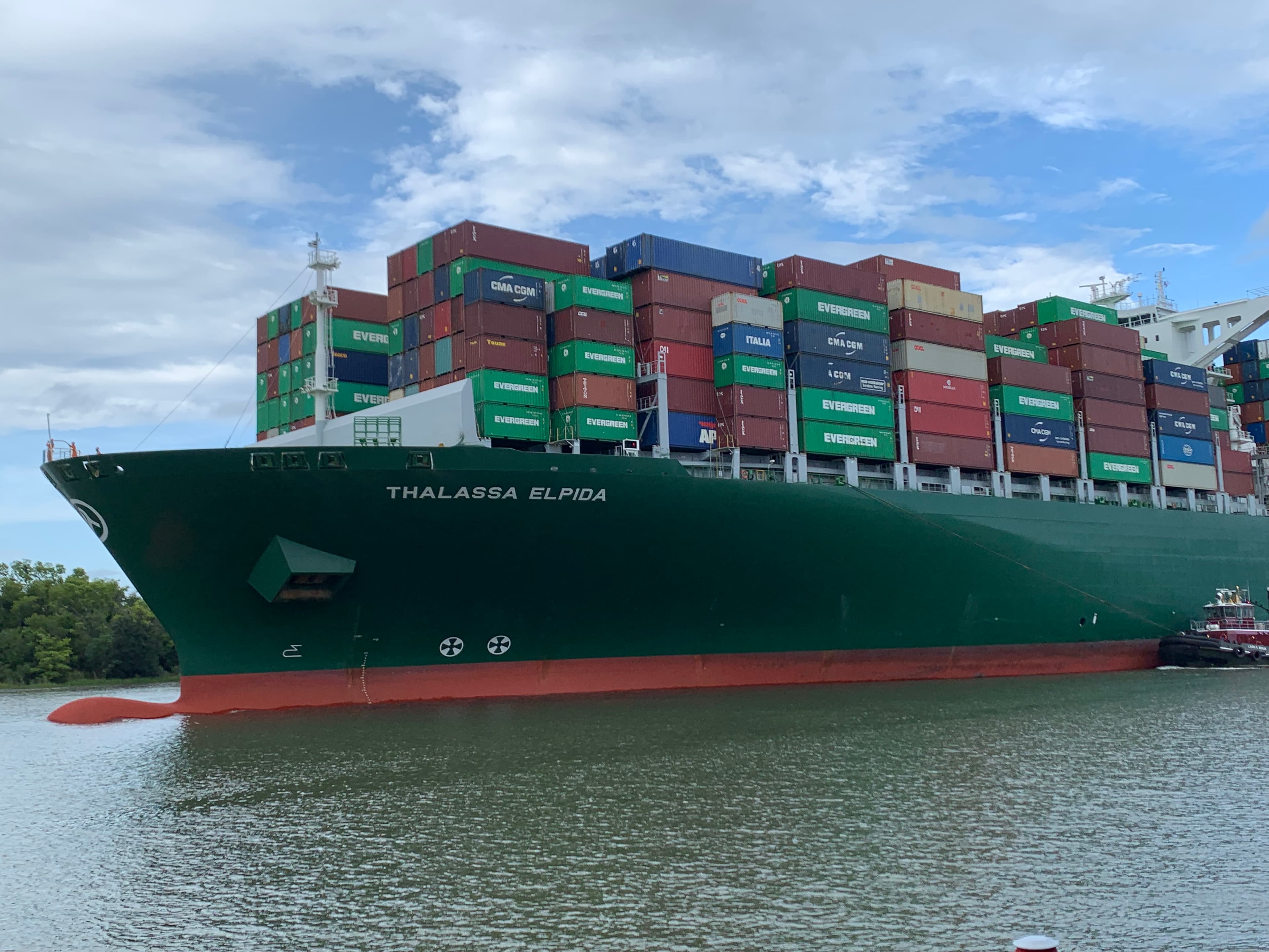 Large green container ship Thalassa Elpida loaded with colorful containers sailing on a river.