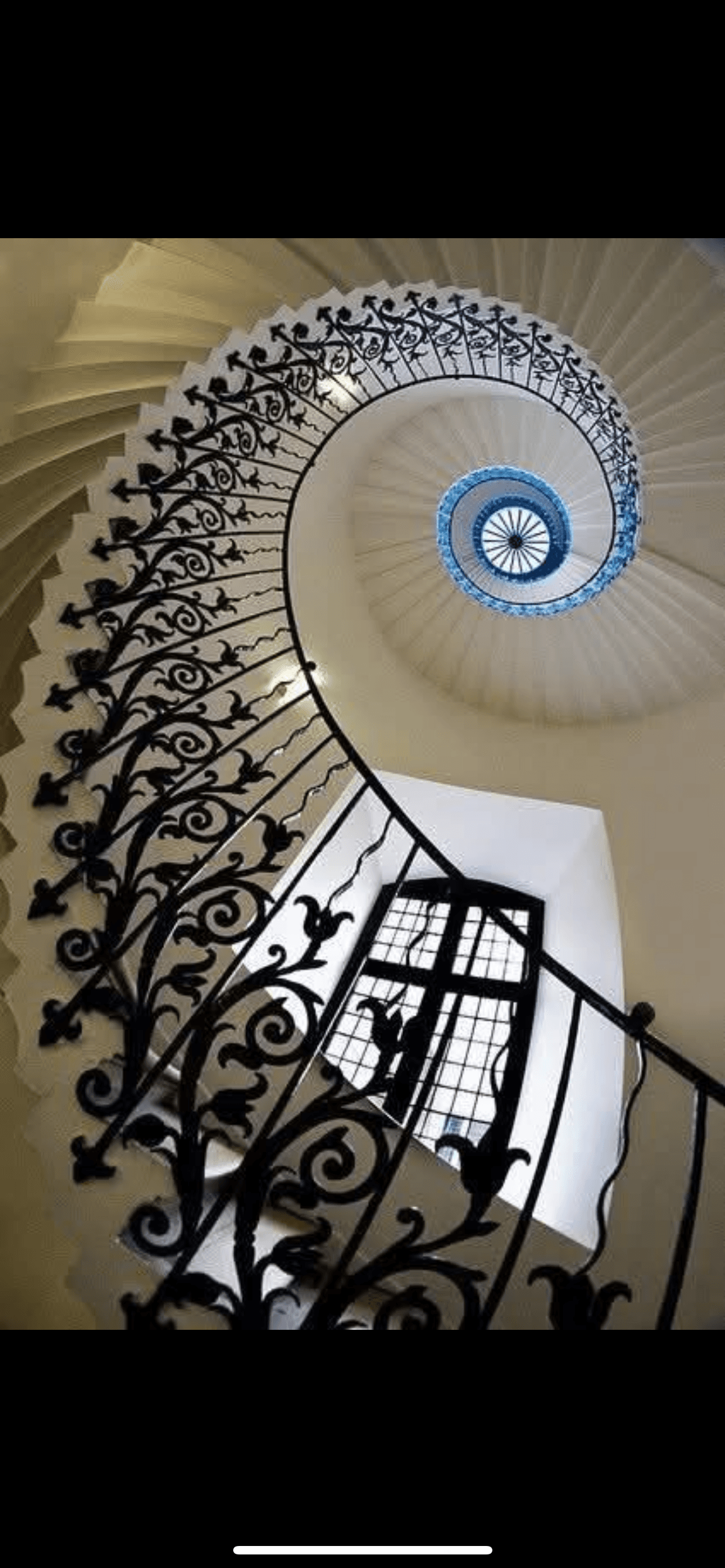 Ornate black iron railings spiral upward on a white staircase toward a blue circular skylight.